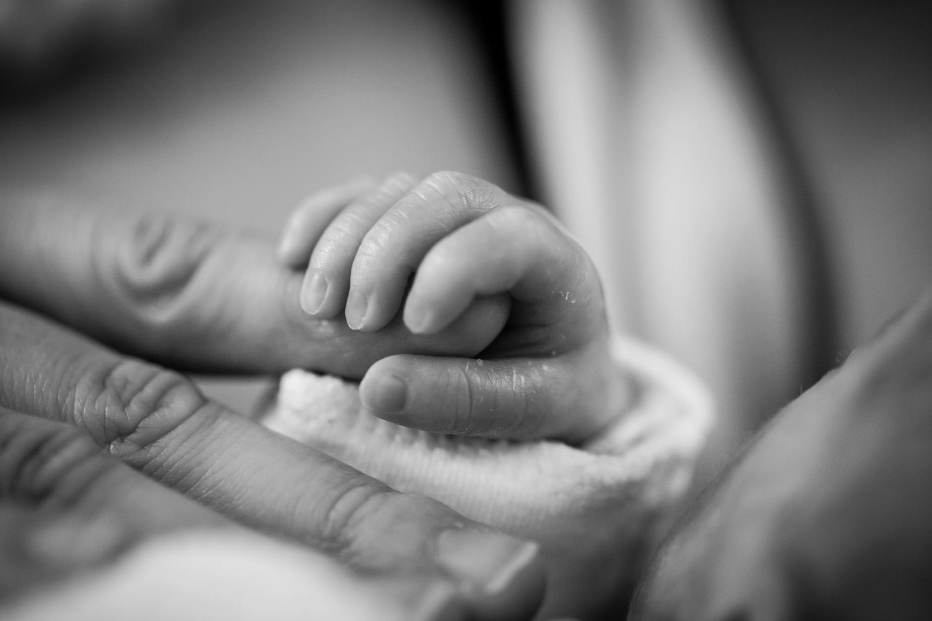 grayscale photography of baby holding finger