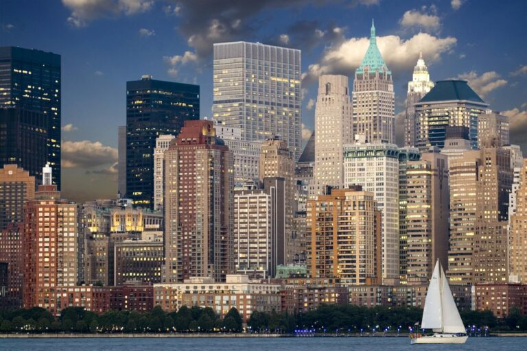 cityscape during nighttime near body of water and sail boat