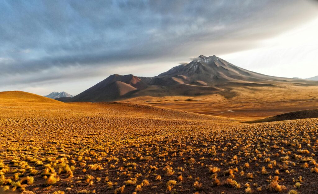 brown field near mountain under cloudy sky