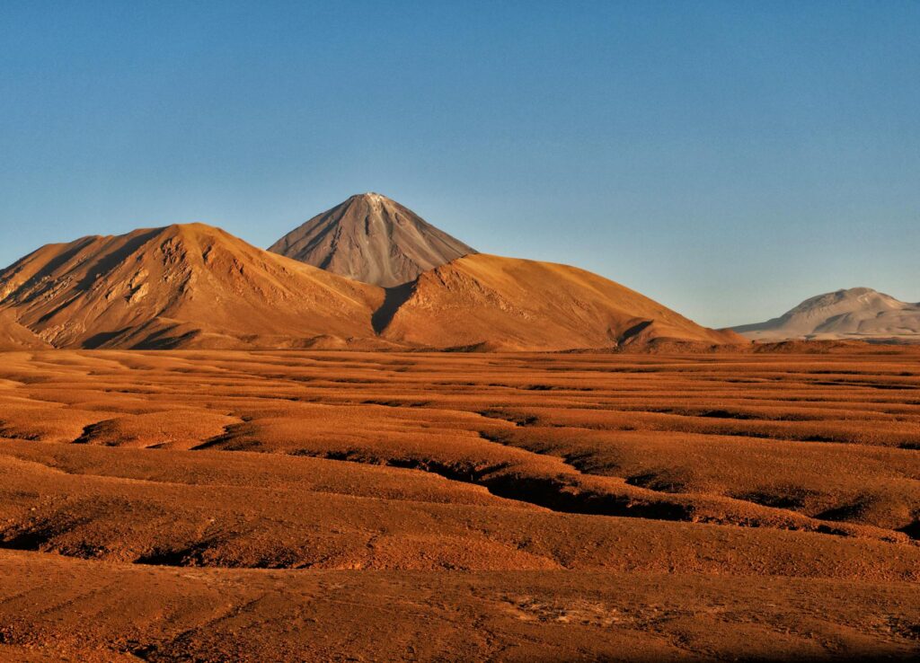 brown sand near brown mountains under blue sky