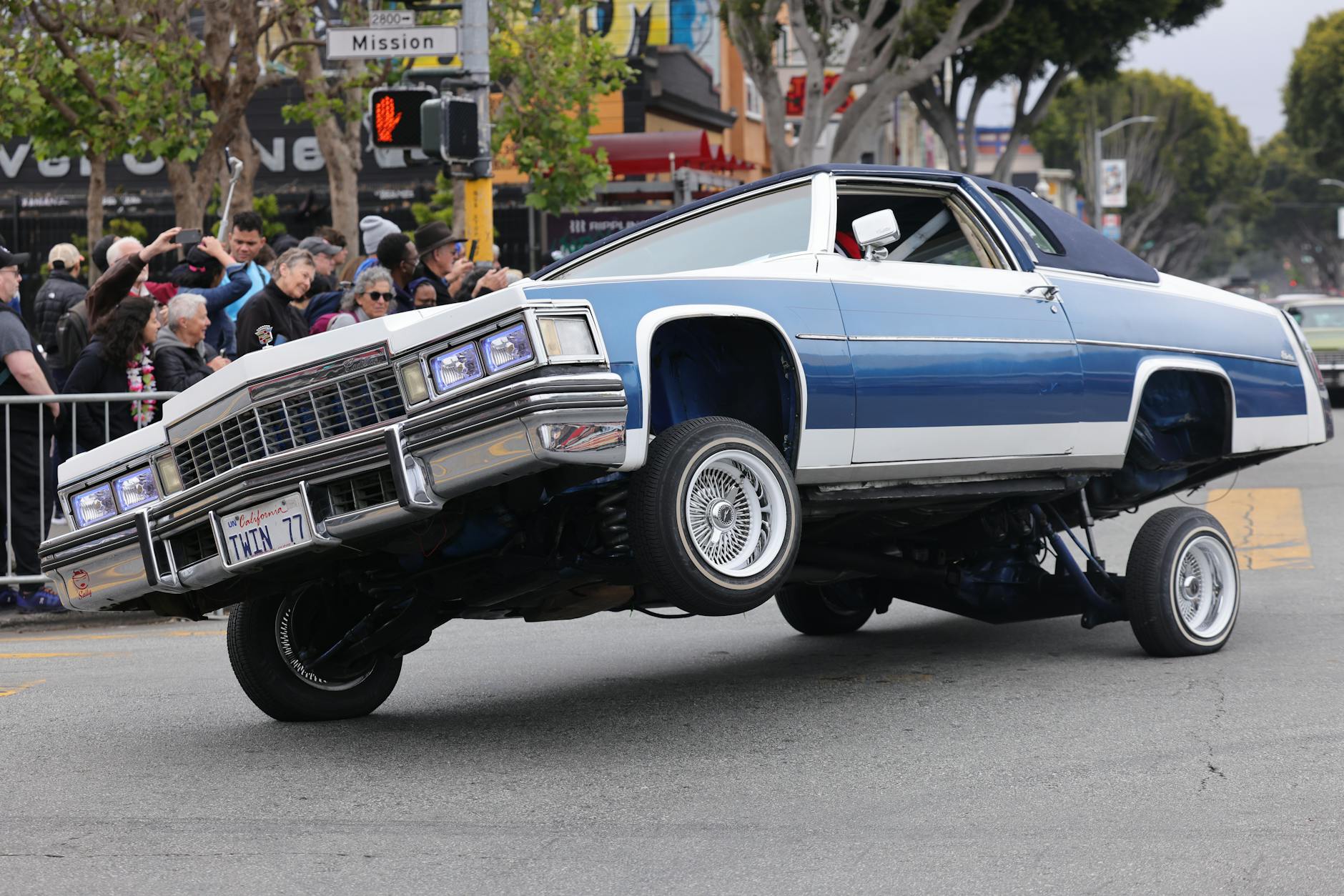 people watching a lowrider cadillac on the street